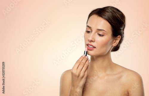 beauty, makeup and cosmetics concept - happy smiling young woman with pink lipstick over beige background