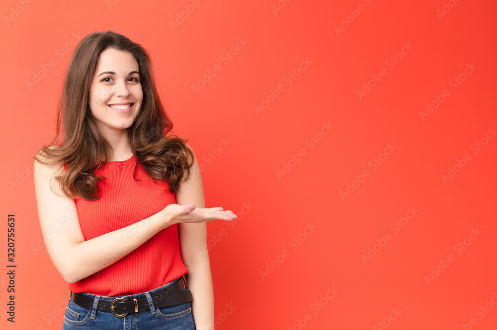 young pretty woman smiling cheerfully, feeling happy and showing a concept in copy space with palm of hand against red wall - obrazy, fototapety, plakaty 