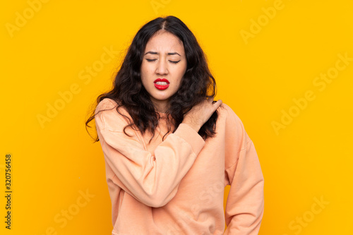 Spanish Chinese woman over isolated yellow background suffering from pain in shoulder for having made an effort © luismolinero