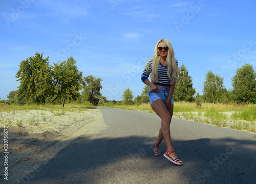A young woman in a striped blue t-shirt stands on an asphalt road in nature. © YAROSLOVEPHOTOVIDEO