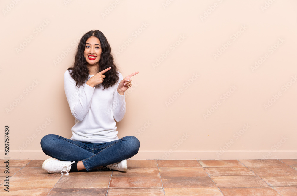Young woman sitting on the floor frightened and pointing to the side Young woman sitting on the floor frightened and pointing to the side