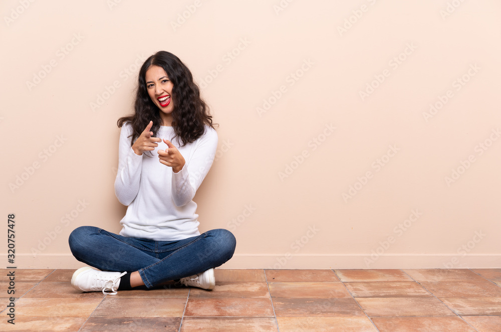 Young woman sitting on the floor pointing to the front and smiling