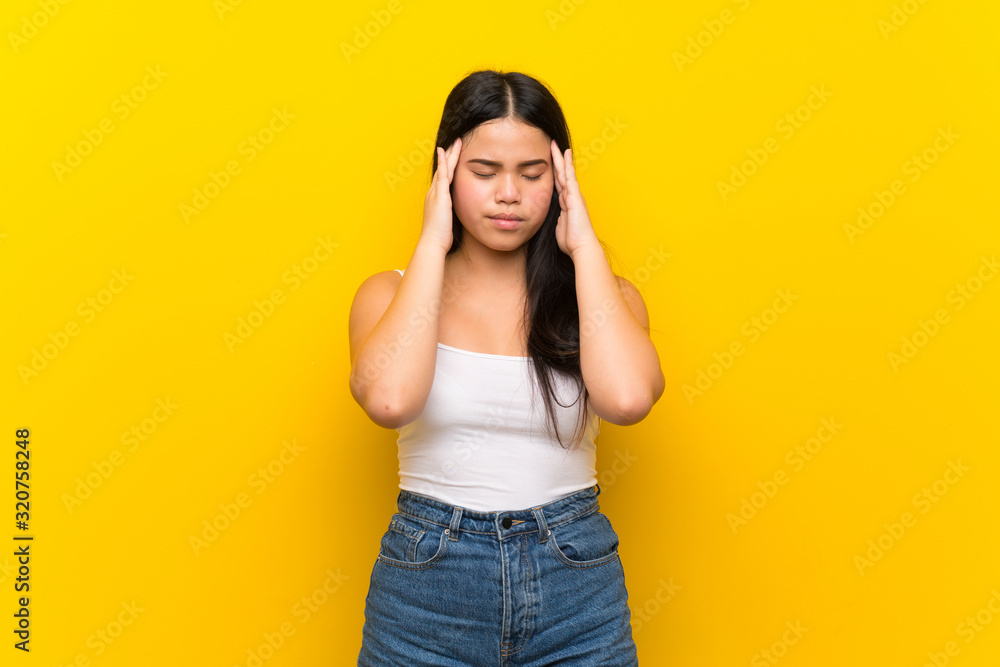 Young teenager Asian girl over isolated yellow background with headache Young teenager Asian girl over isolated yellow background with headache