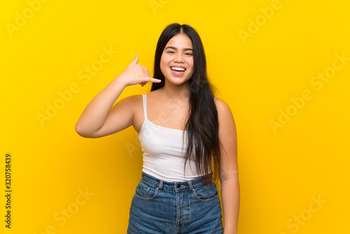 Young teenager Asian girl over isolated yellow background making phone gesture. Call me back sign