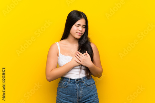 Young teenager Asian girl over isolated yellow background having a pain in the heart © luismolinero