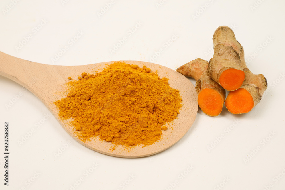 Turmeric powder in a wooden spoon and turmeric root extracted on a white background, used as a tonic for the body and food ingredients. Turmeric powder in a wooden spoon and turmeric root extracted on a white background, used as a tonic for the body and food ingredients.