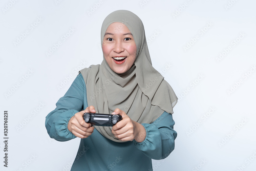 Asian Muslim woman playing console with wireless controller. Asian Muslim woman playing console with wireless controller.