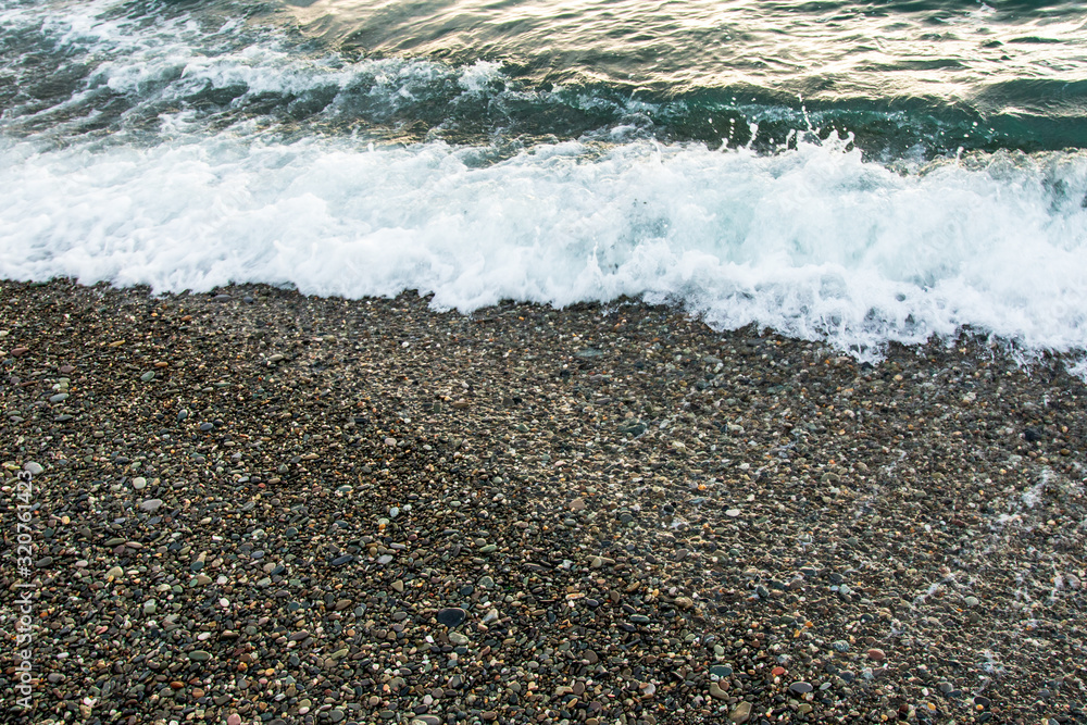 The wave rolls onto the seashore, which is covered with small stones The wave rolls onto the seashore, which is covered with small stones
