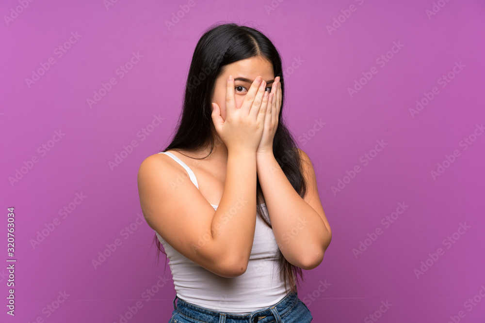 Young teenager Asian girl over isolated purple background covering eyes and looking through fingers Young teenager Asian girl over isolated purple background covering eyes and looking through fingers
