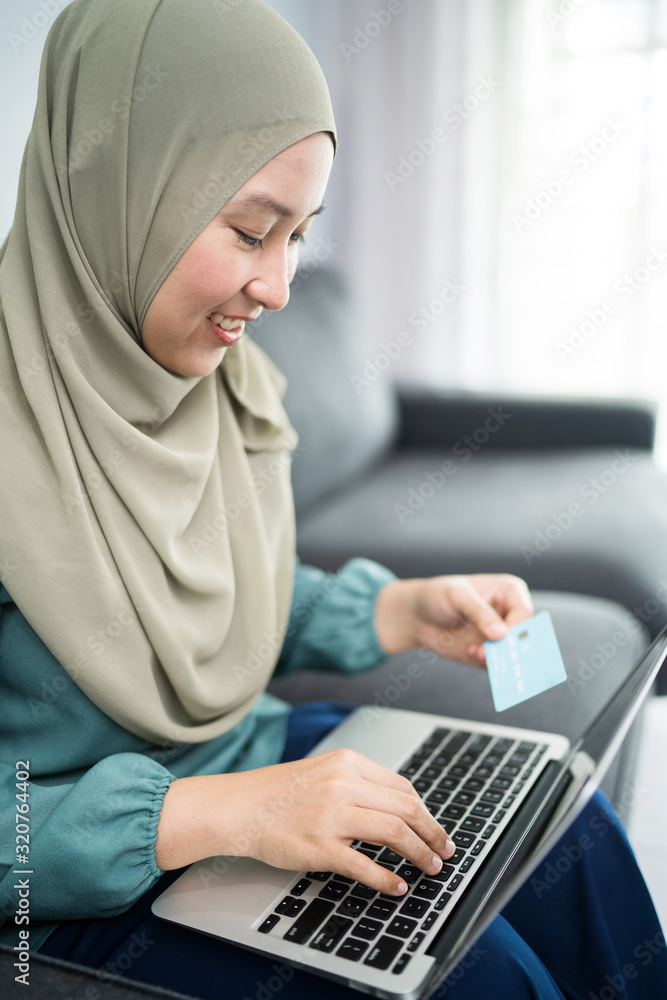 Female muslim woman using laptop while holding credit card. Female muslim woman using laptop while holding credit card.