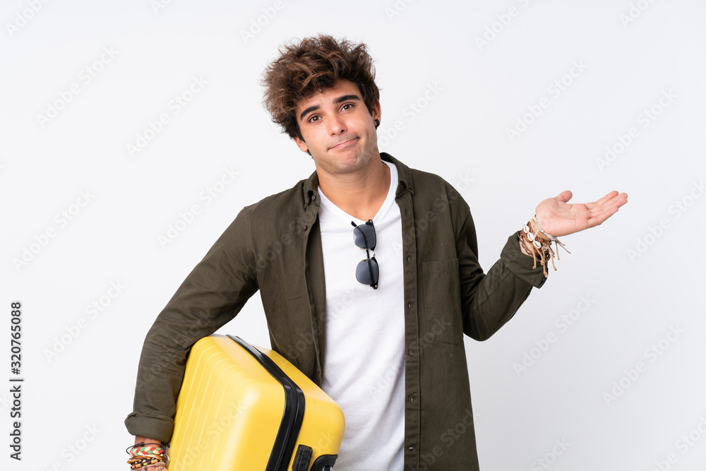 Young Traveler man holding a suitcase over isolated white background having doubts with confuse face expression Young Traveler man holding a suitcase over isolated white background having doubts with confuse face expression