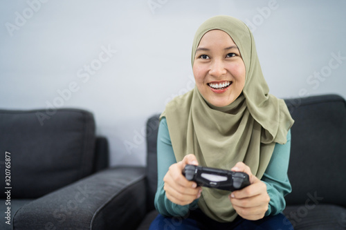 Beautiful muslim woman playing console games at her couch.