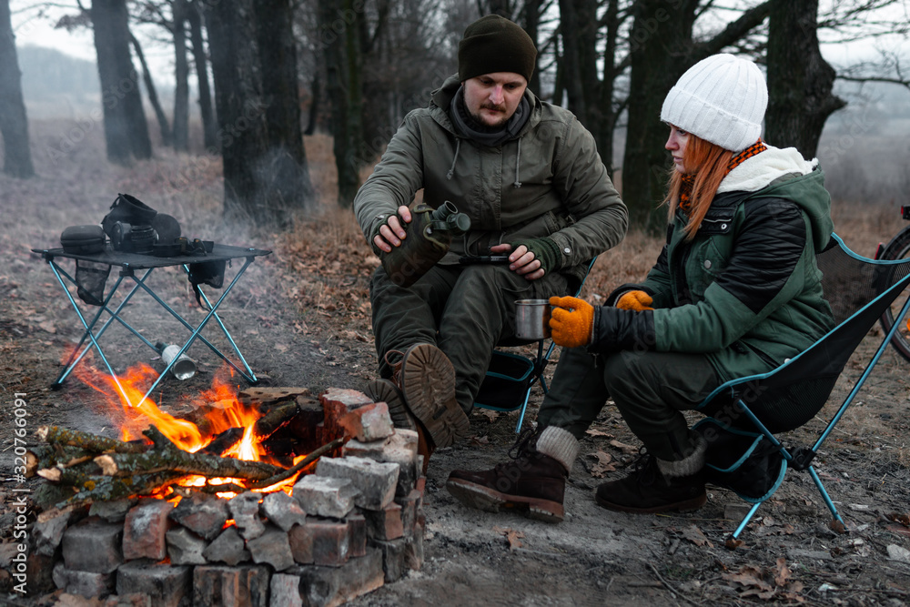 A couple of people are sitting on light chairs by the fire. Cold autumn evening in the forest. The concept of an active lifestyle, travel, vacation. warm their hands at the campfire A couple of people are sitting on light chairs by the fire. Cold autumn evening in the forest. The concept of an active lifestyle, travel, vacation. warm their hands at the campfire