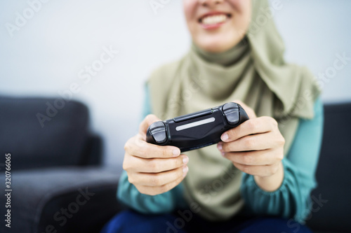 Beautiful muslim woman playing console games at her couch.