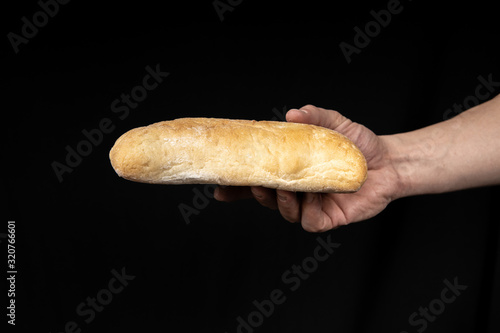 Fresh bread ciabatta in the male hand on black background.