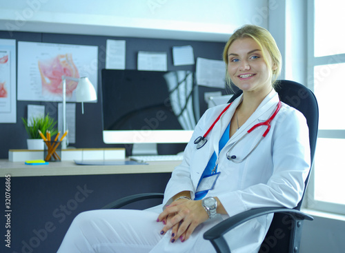 Confident female doctor sitting at office desk and smiling at camera