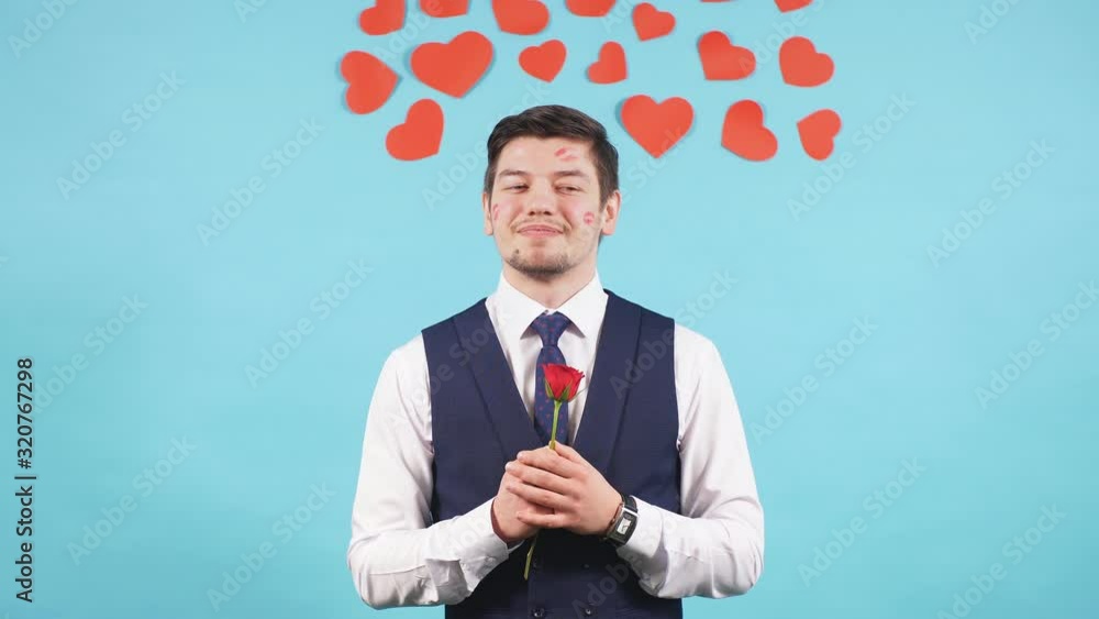 Young bearded caucasian male in tuxedo stand with red flower isolated over blue background. Handsome guy gentleman waiting for his girlfriend, love concept Young bearded caucasian male in tuxedo stand with red flower isolated over blue background. Handsome guy gentleman waiting for his girlfriend, love concept
