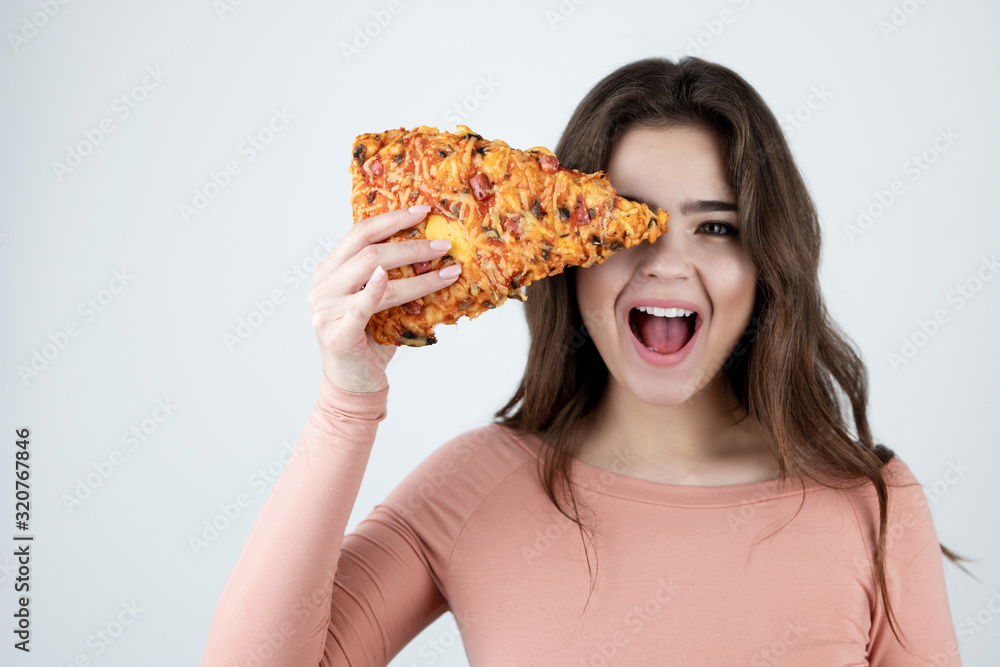 young beautiful woman holding slice of pizza in one hand near her face looking happy being on diet isolated white background