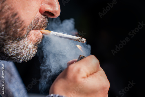 Close up of bearded man holding a lighter and smoking a cigarette on black background. photo