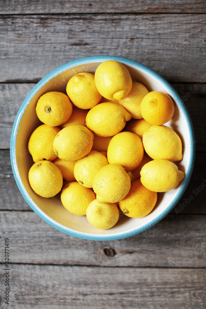 yellow lemons in a glass bowl on wooden background
