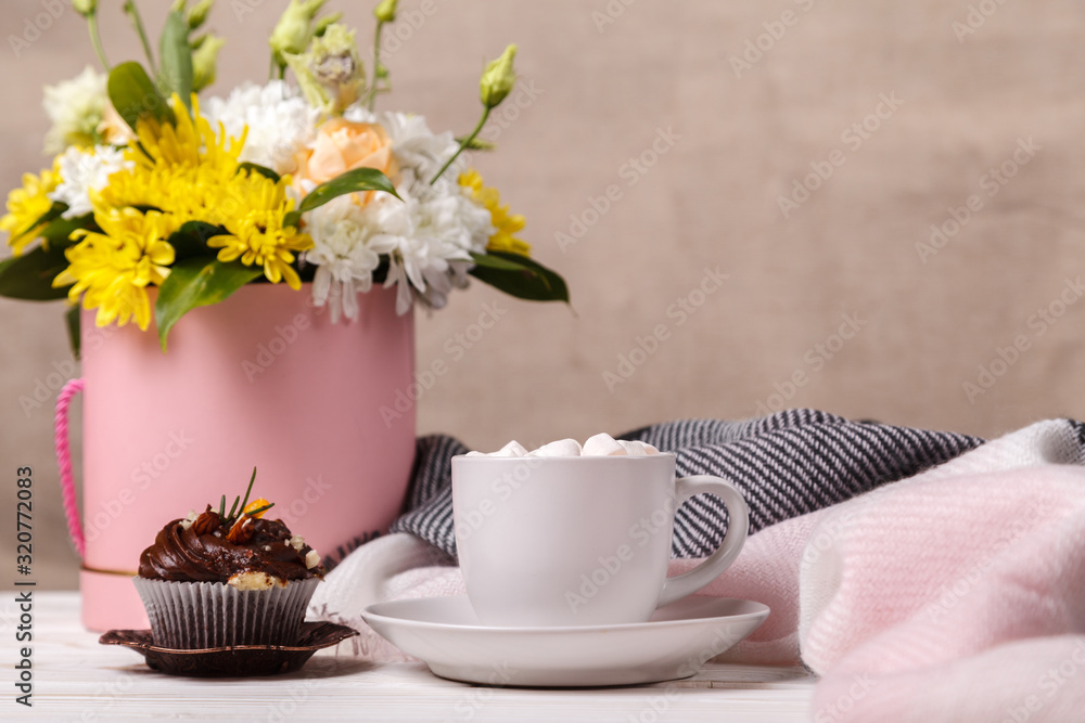 Cup of cocoa with marshmallows, a cupcake, a bouquet of flowers and a soft blanket in the background. Pleasant awakening