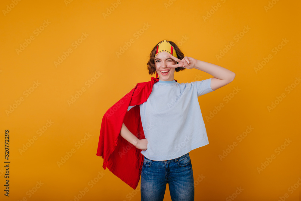 Stylish lady in funny paper crown posing with peace sign. Indoor photo of good-looking curly girl in princess costume. Stylish lady in funny paper crown posing with peace sign. Indoor photo of good-looking curly girl in princess costume.