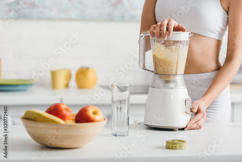 Cropped view of sportswoman preparing smoothie near measuring tape on kitchen table