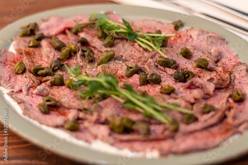 Beef cooked in suvid. It is cut into thin slices and decorated with capers and microgreen. On a wooden background in an oval dish.