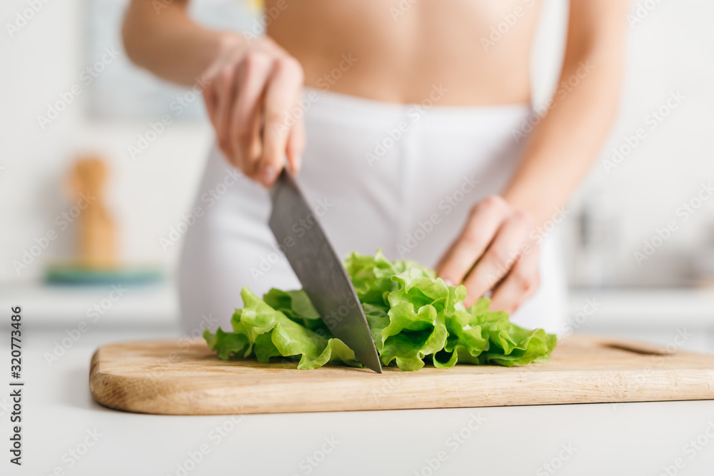 Selective focus of slim woman cutting fresh lettuce on kitchen table