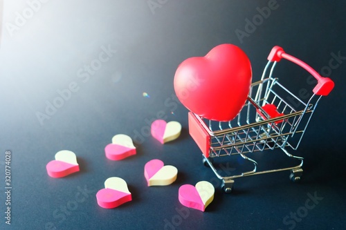 Red rubber heart in small shopping cart with many two tone red and white placed spread on black background. Giving of delivering of love, care, concern, safety, volunteer, celebrate of valentine's day