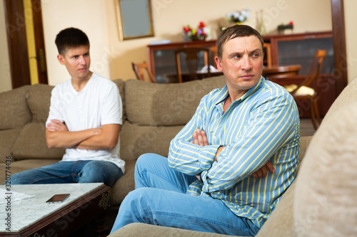 Upset father sitting while quarreling with his teenage son