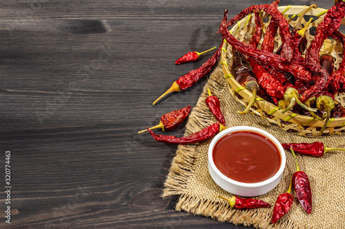 Hot chili sauce in bowl with different varieties of dry hot peppers, main ingredient for preparation. Black wooden cooking background