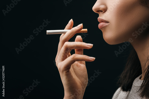 Fotografie Side view of woman holding cigarette isolated on black