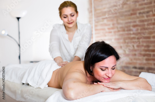 Professional masseuse is doing massage of back and loin to adult woman