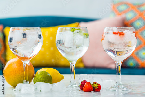 Three gin tonic cocktails with strawberries, lime and blueberries.