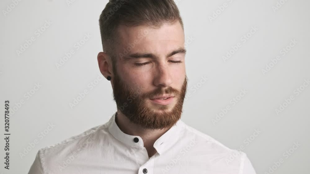 A calm bearded man wearing white shirt is opening his eyes to the camera isolated over white wall background A calm bearded man wearing white shirt is opening his eyes to the camera isolated over white wall background