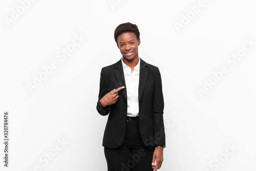 young pretty black womanlooking proud, confident and happy, smiling and pointing to self or making number one sign against white wall photo