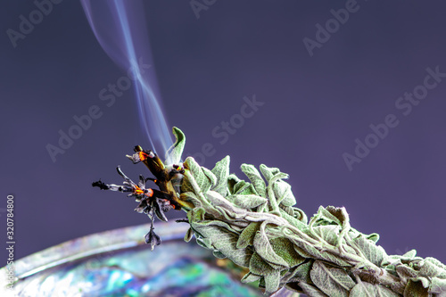 Smudge stick close-up shot. Burning / smudging sage stick on dark background. Native American tradition, using for removing negative energies. photo