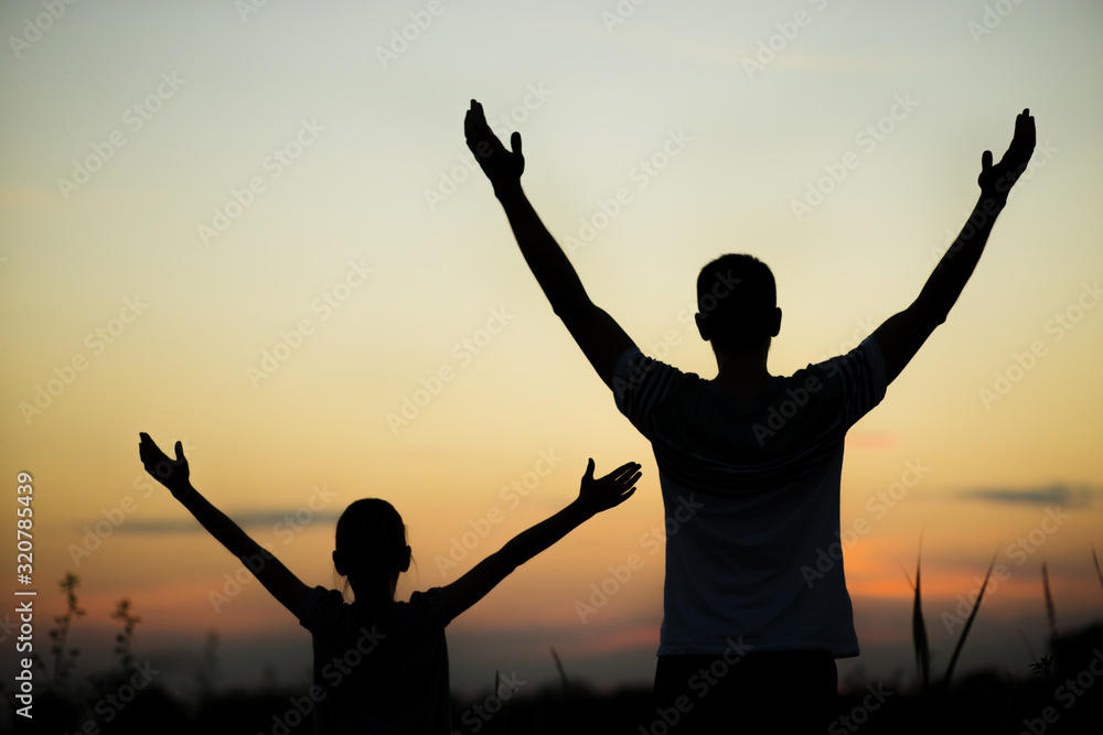 Silhouettes of father and daughter on his shoulders with hands up having fun, against sunset sky. Parenthood, family activities, support and love themes