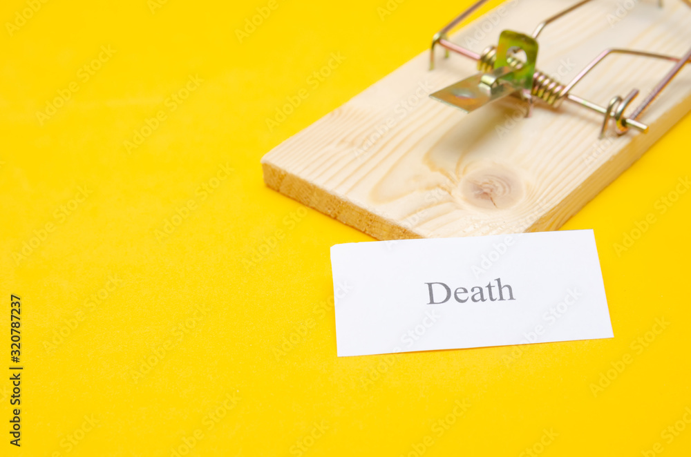 mousetrap with a piece of paper and the inscription Death on a yellow background with a copy space. concept or idea mousetrap with a piece of paper and the inscription Death on a yellow background with a copy space. concept or idea