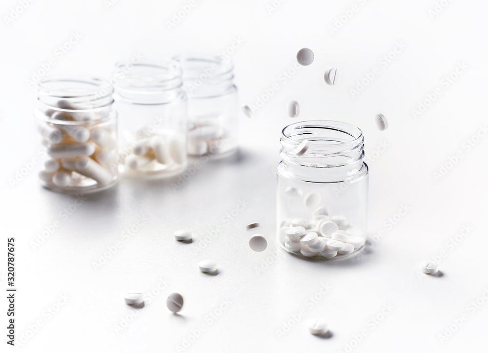 White round pills fly into a jar of pills. White background. Flying objects. Health concept. White round pills fly into a jar of pills. White background. Flying objects. Health concept.