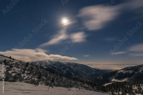the moon shines on the snowy landscape of the mountains and clouds fly on the horizon