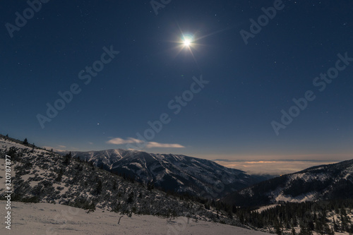 the moon shines on the snowy landscape of the mountains and clouds fly on the horizon