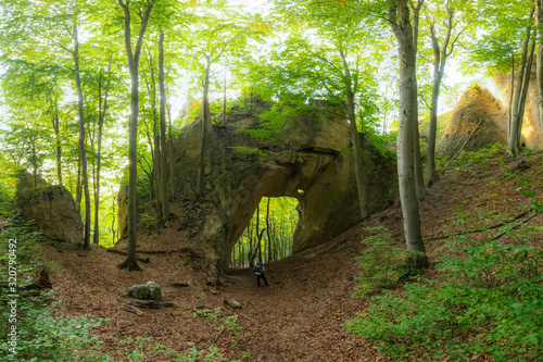 A hiker is small under a natural stone gate in the middle of a forest