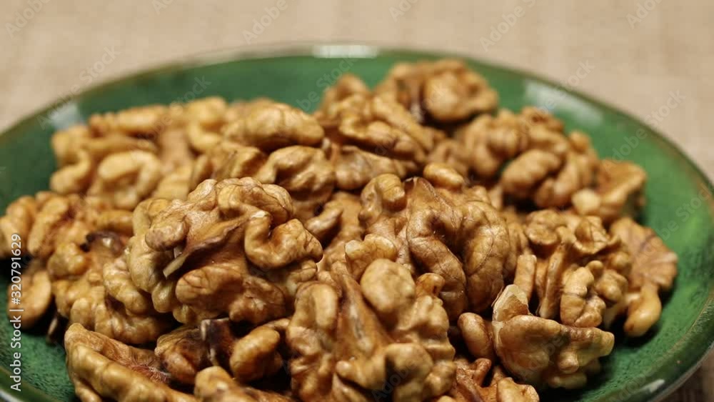 A green plate with walnuts is placed on a gray wicker surface, close-up A green plate with walnuts is placed on a gray wicker surface, close-up