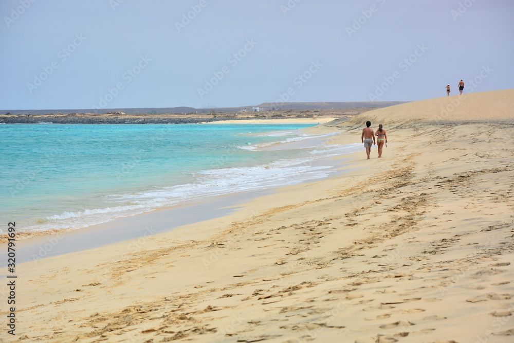 A couple walking on a sandy beach, a blue turquoise ocean, sea A couple walking on a sandy beach, a blue turquoise ocean, sea