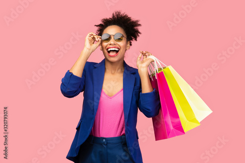 Excited black woman holding shopping bags at pink studio photo