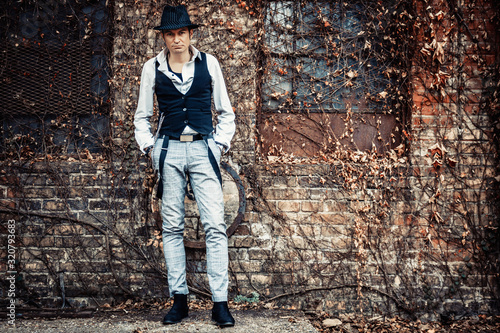 Full length of retro-styled man with a hat against brick wall.