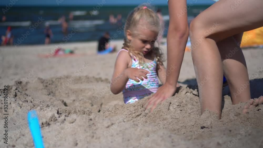 Attractive woman digging little girl deep in sand. Mother and daughter have fun Attractive woman digging little girl deep in sand. Mother and daughter have fun