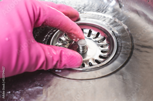 Man in pink glove plugs cork in sink for dishwashing. Save water